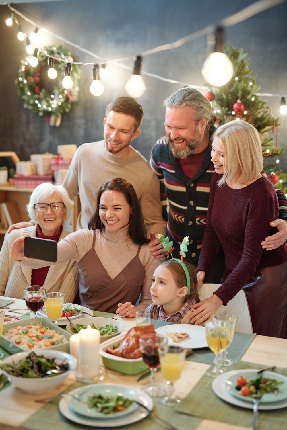 joyful-family-six-looking-smartphone-held-by-young-woman-while-making-selfie-by-served-festive-table-home (1)