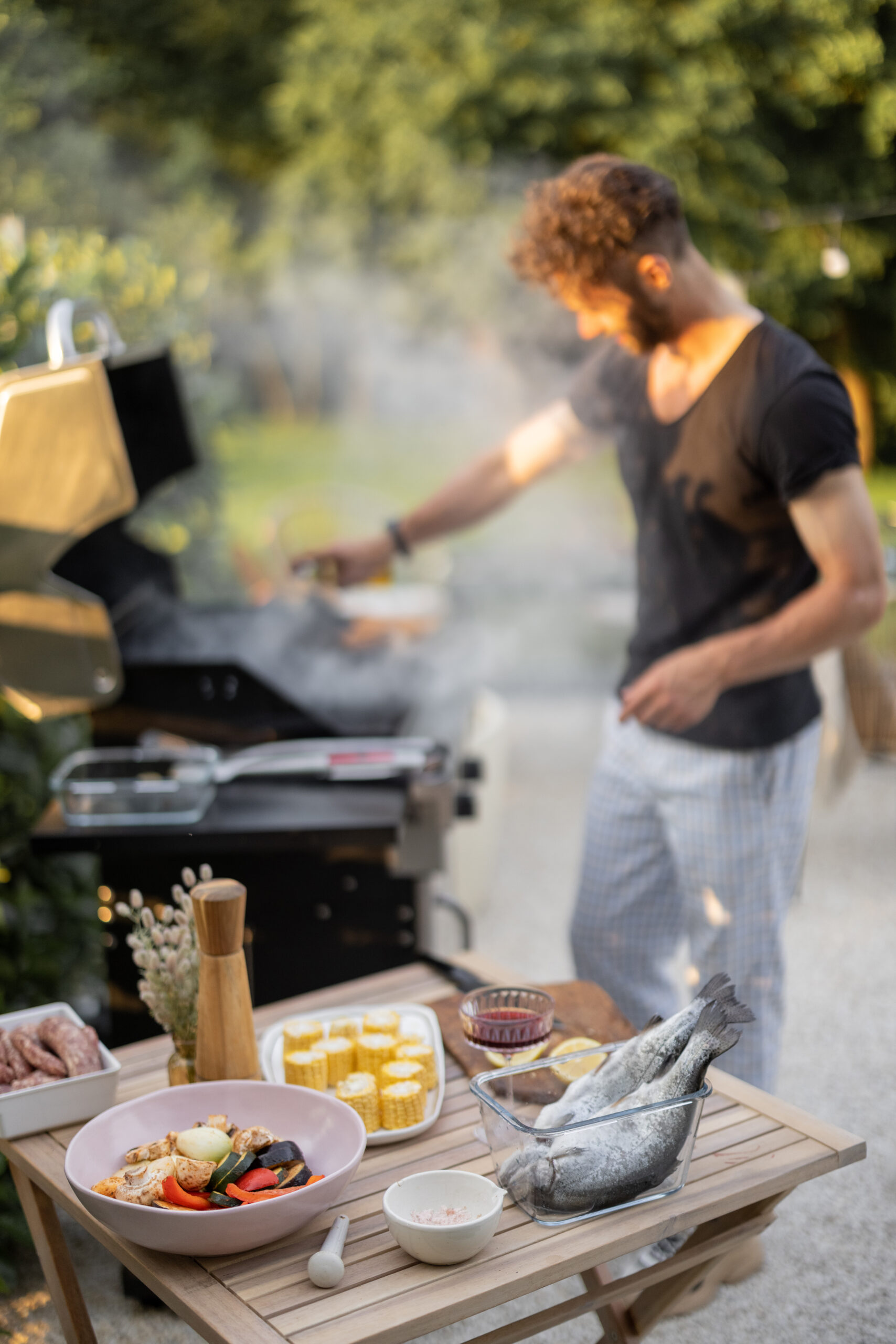 Men preparing fish for a grill, cooking healthy sea food and vegetables on a modern gas grill at backyard on nature. Food ingredients on the background